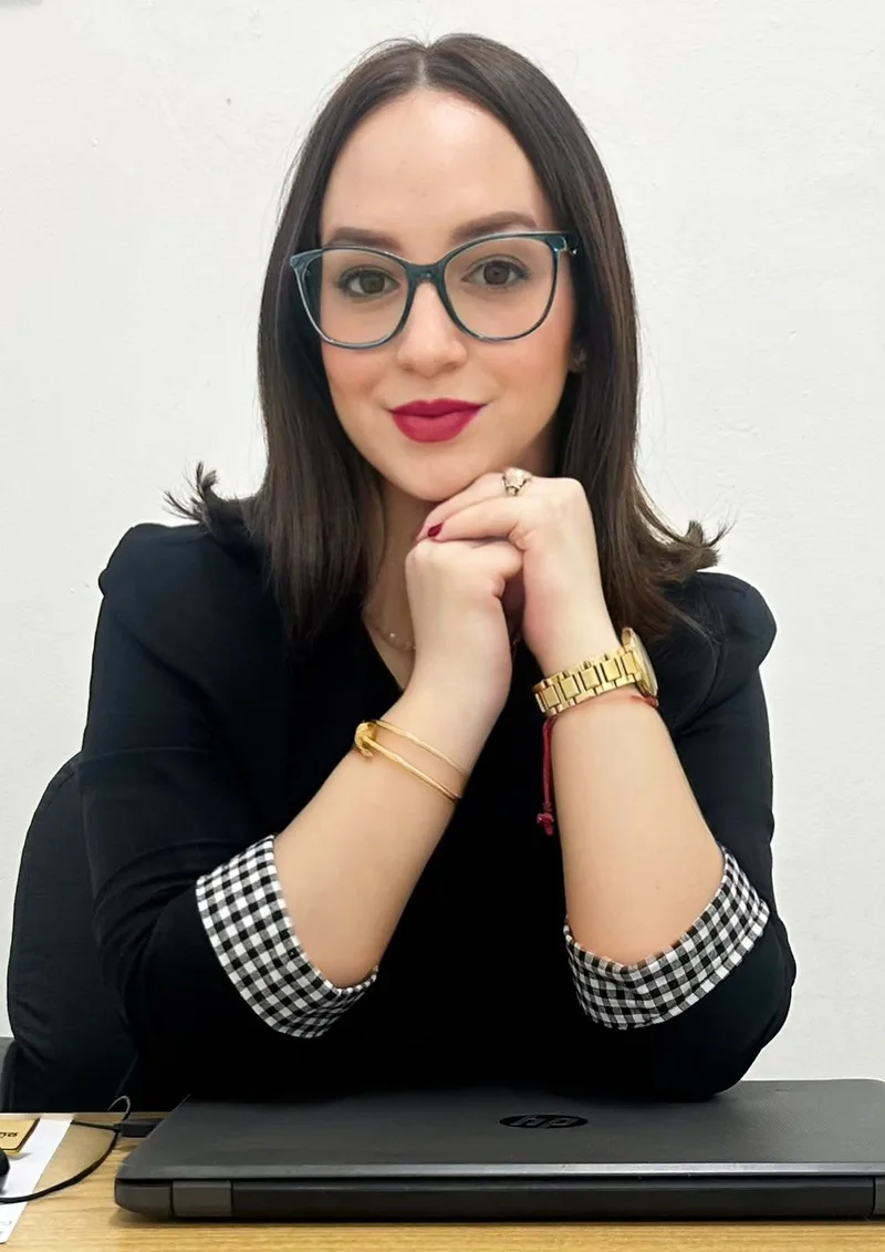 Luisa M. Reyes P. sentada en su escritorio, sonriendo, con las manos juntas bajo la barbilla